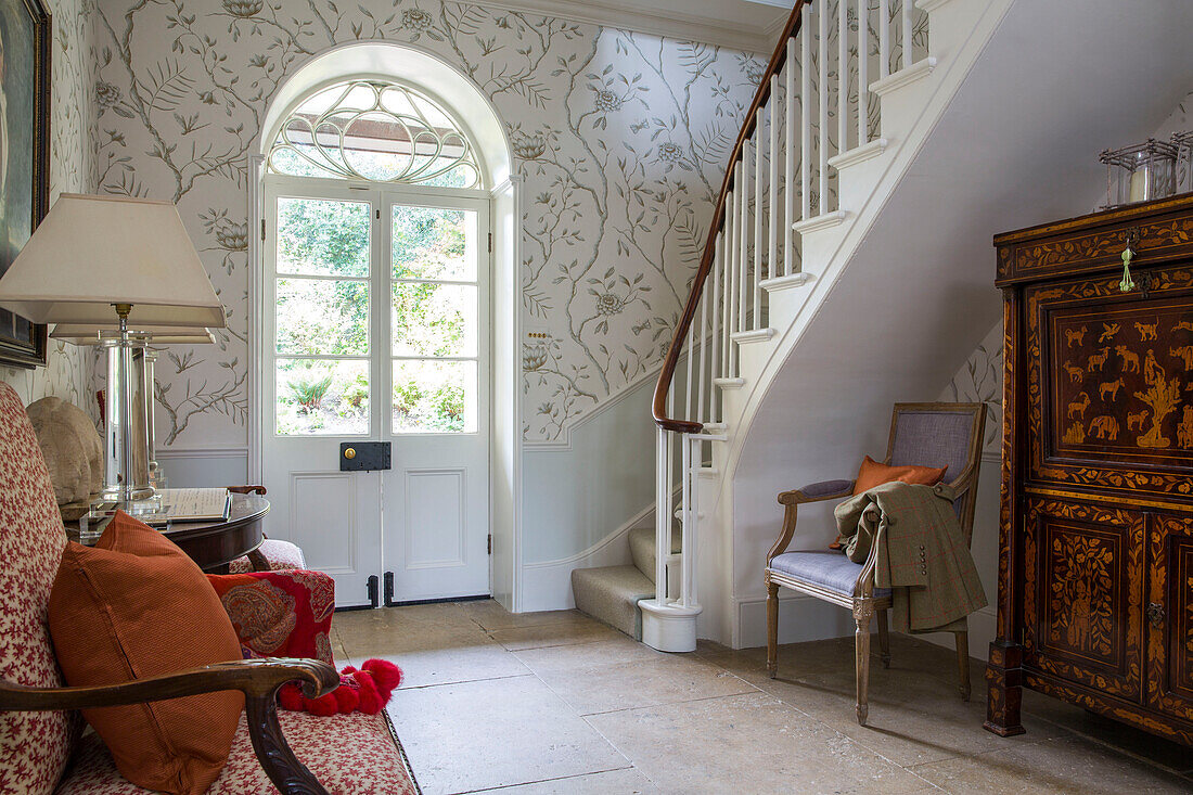 Patterned wallpaper and flagstone floor with marquetry cabinet in Georgian rectory hallway Northamptonshire England UK