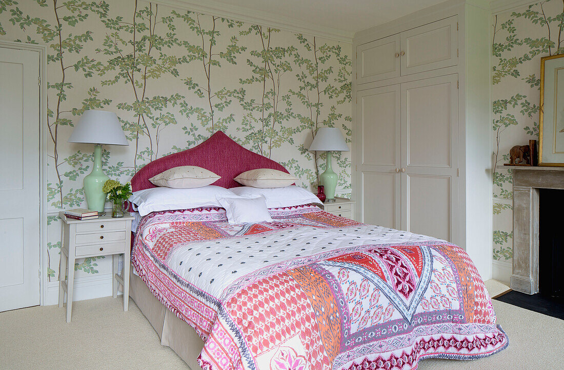 Quilted cover on double bed with leaf patterned wallpaper in Georgian rectory Northamptonshire England UK