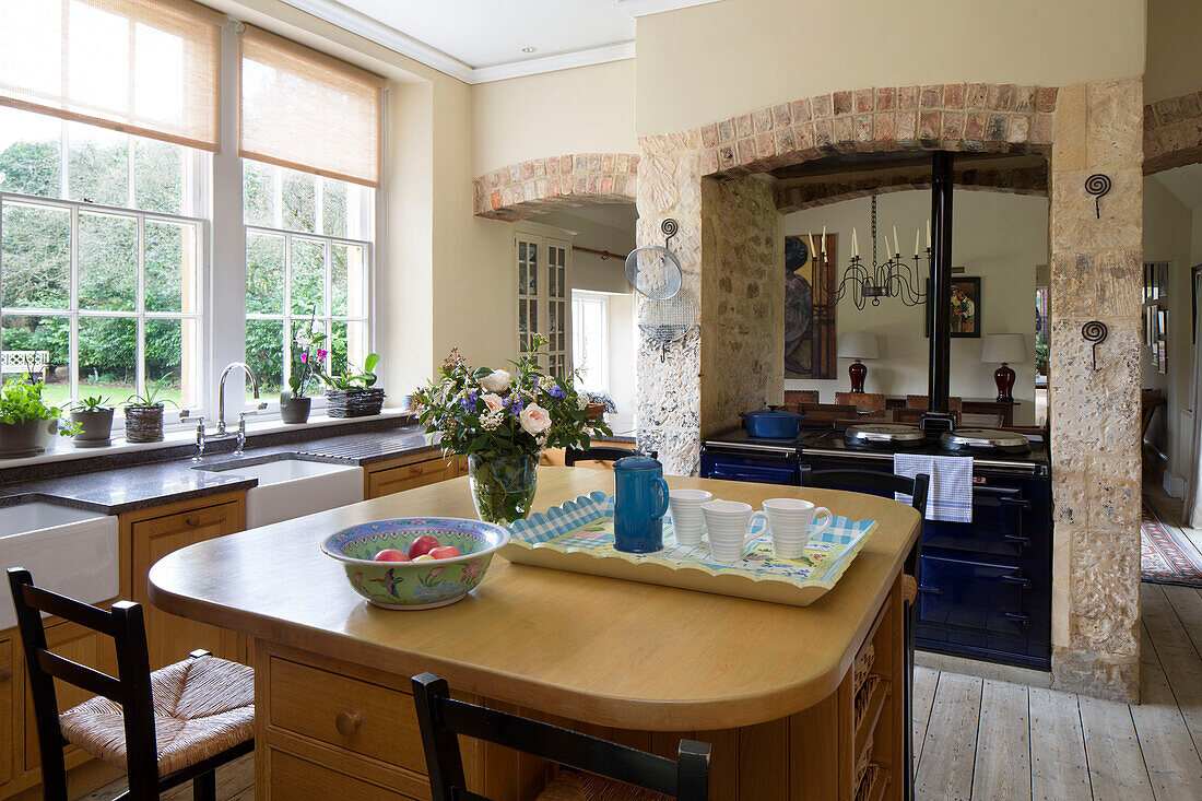 Hölzerne Kücheninsel mit dunkelblauem Herd und Blick auf den angrenzenden Raum in einem Bauernhaus in Gloucestershire, England, UK