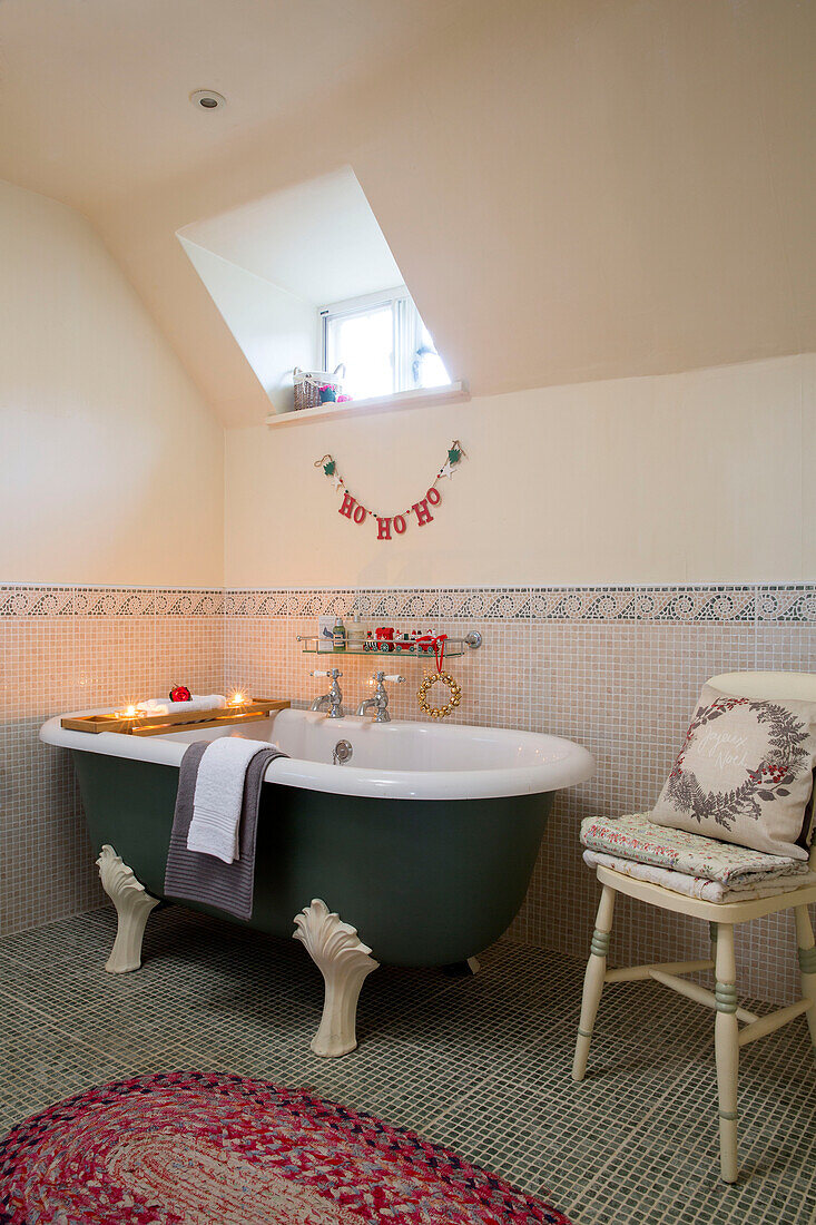 Freistehende Badewanne unter Dachfenster in mosaikgefliestem Badezimmer in Bauernhaus in Hampshire, England UK