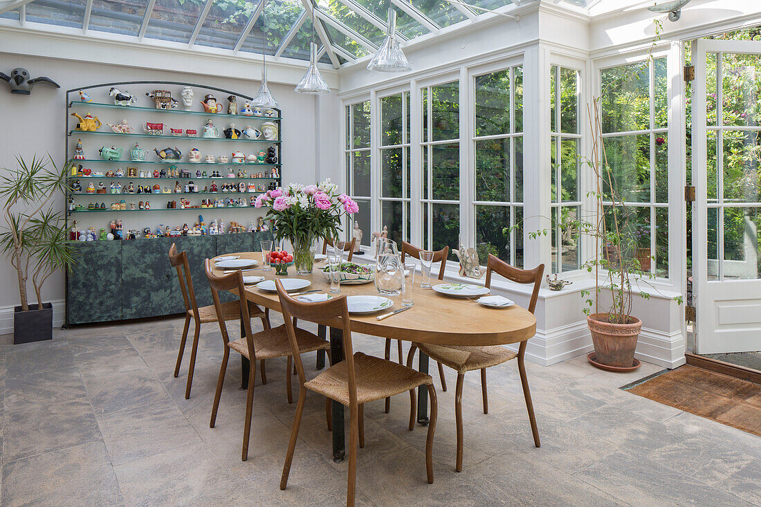 Wooden dining table and chairs with collection of kitchenware in conservatory extension of London townhouse UK