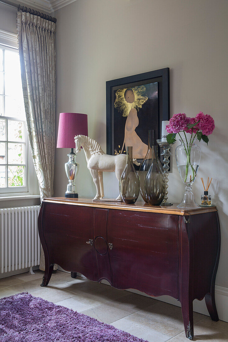 Pink flowers and lamp on vintage sideboard with artwork and sculpture in detached Sussex country house UK