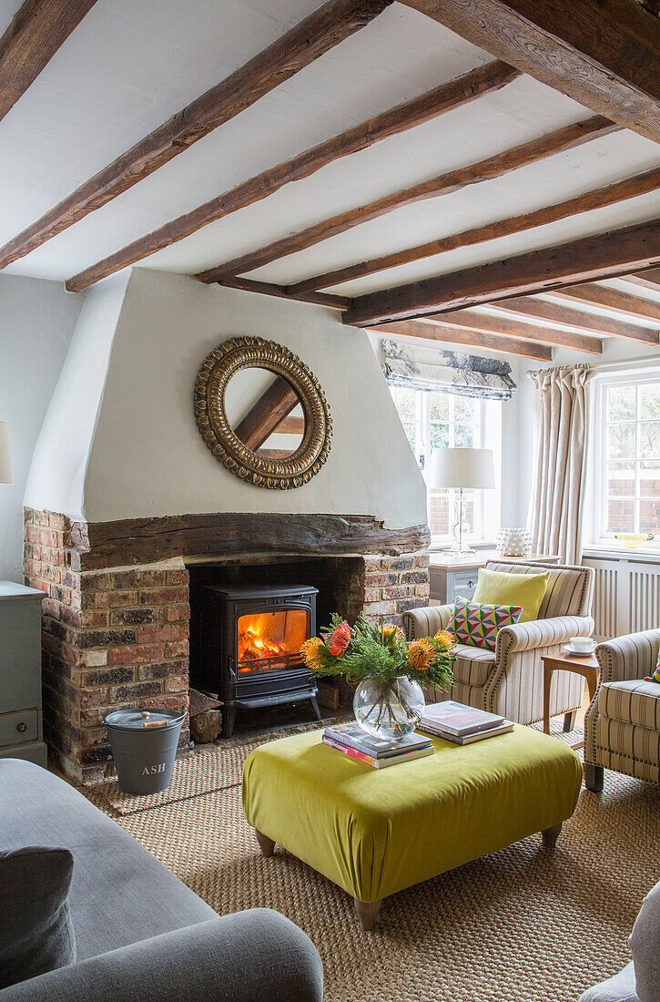 Cut flowers on yellow ottoman with lit woodburner in Oast house conversion Kent UK