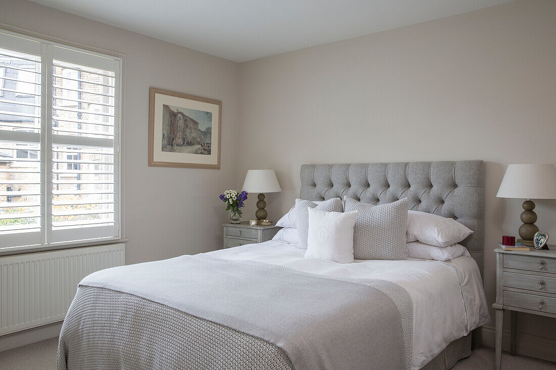 Pair of lamps and light grey headboard with bed covers at window in London townhouse UK