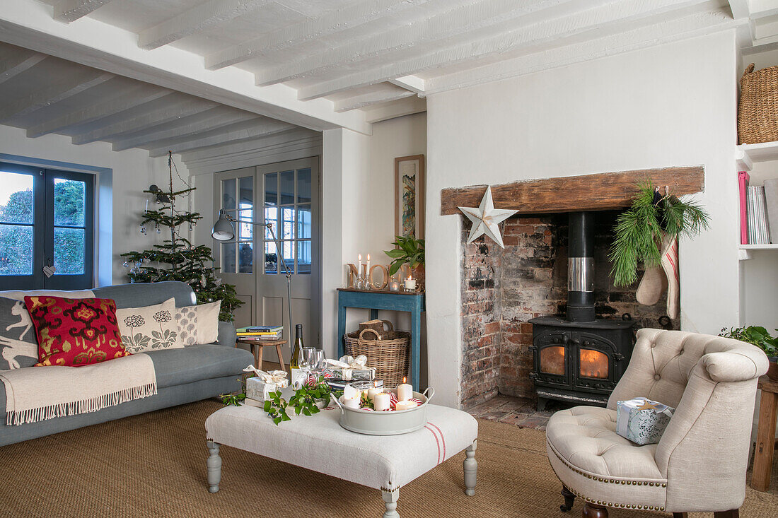 Beleuchteter Kaminofen und weiße Ottomane mit grauem Sofa in einem Bauernhaus in West Sussex UK