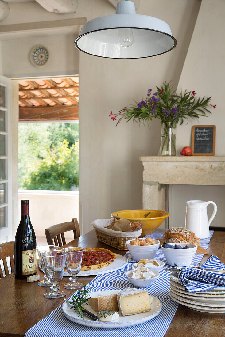 Weiße Pendelleuchte über einem gedeckten Tisch mit Speisen und Getränken in einem provenzalischen Bauernhaus aus dem 19