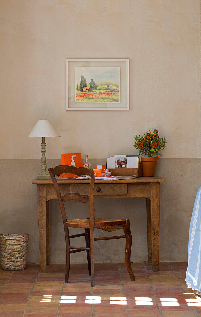 Buchstabenständer und Lampe auf dem Schreibtisch unter einem Kunstwerk mit sonnenbeschienenem Terrakottaboden in einem provenzalischen Bauernhaus aus dem 19