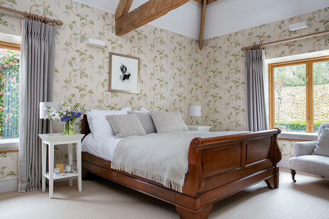 Framed artwork on foliate wallpaper above double sleigh bed in Gloucestershire barn conversion UK
