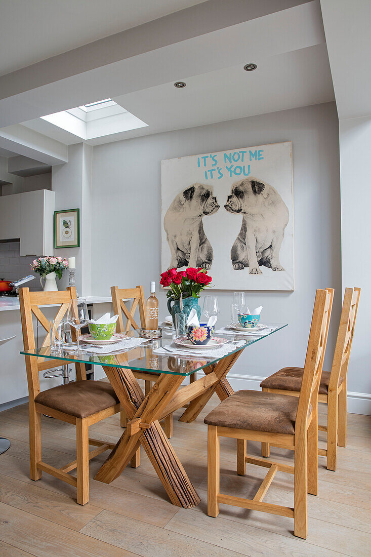 Wooden chairs at glass topped dining table with large artwork of bulldogs in London home UK