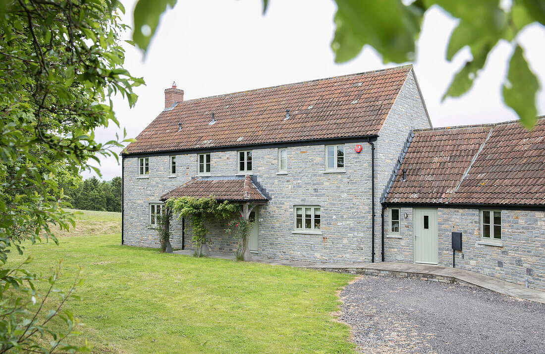 Stone facade with tiled roof and porch of Somerset farmhouse UK