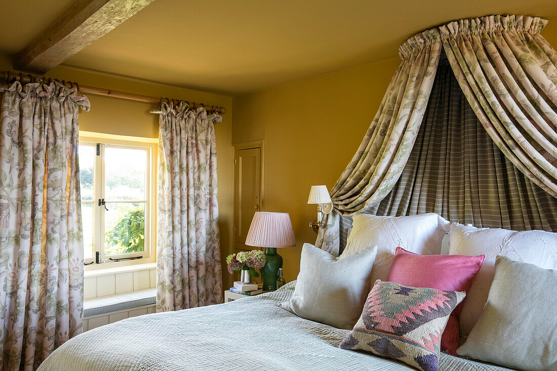 Doppelbett mit farblich abgestimmtem Baldachin am Fenster in einem gelben Zimmer in Somerset, England