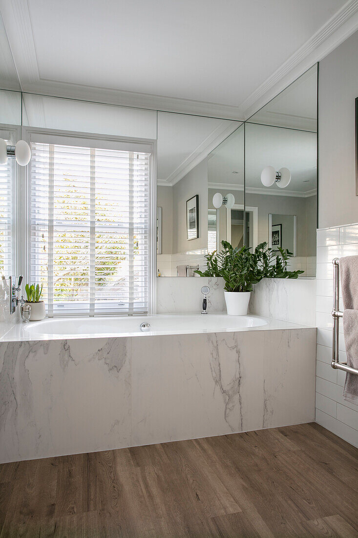 Marble bath with houseplant and corner mirror below window in London home UK