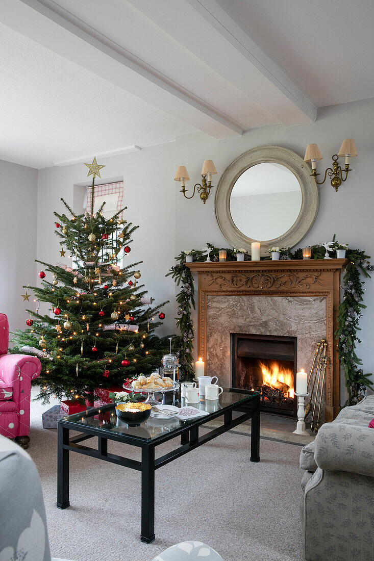 Black coffee table and lit fire with Christmas tree in Arts and Crafts home West Sussex UK