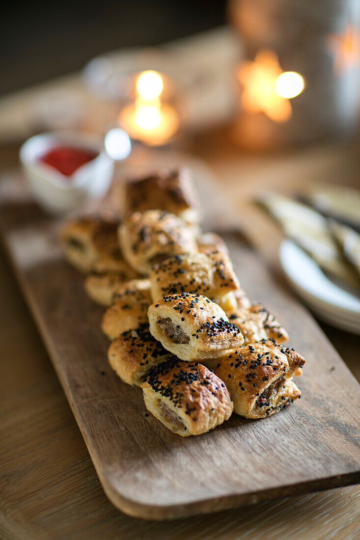 Wurstsemmeln auf einem Holzbrett mit brennenden Kerzen in einem Haus im Arts-and-Crafts-Stil in West Sussex, England