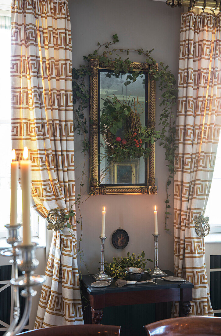 Lit candles on side table with ivy and geometric curtains in Georgian dining room Hertfordshire England UK