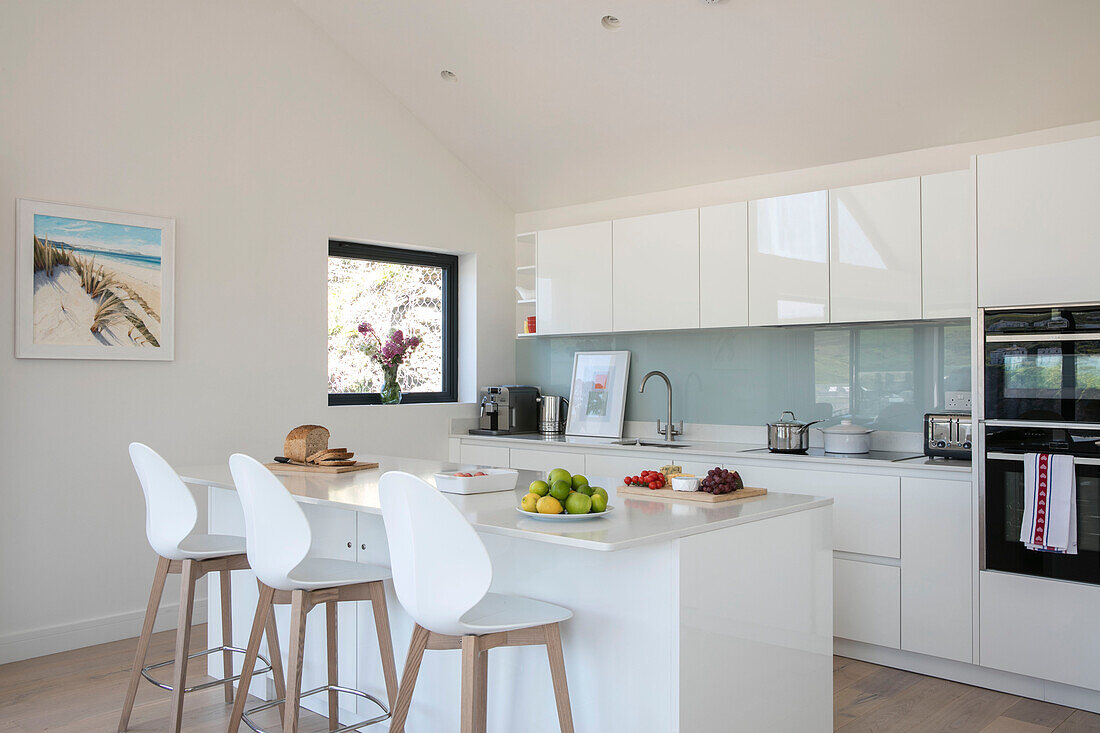 White bar stools at kitchen island with oven and light blue splashback in newbuild Cornwall UK