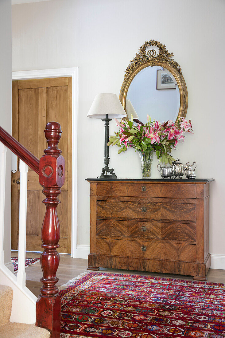 Cut lilies and gilt framed mirror on wooden chest of drawers in hallway of Hampshire home UK