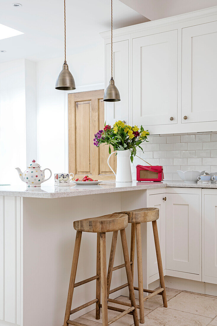 Brass pendant lights above breakfast bar with wooden stools in Hampshire kitchen UK