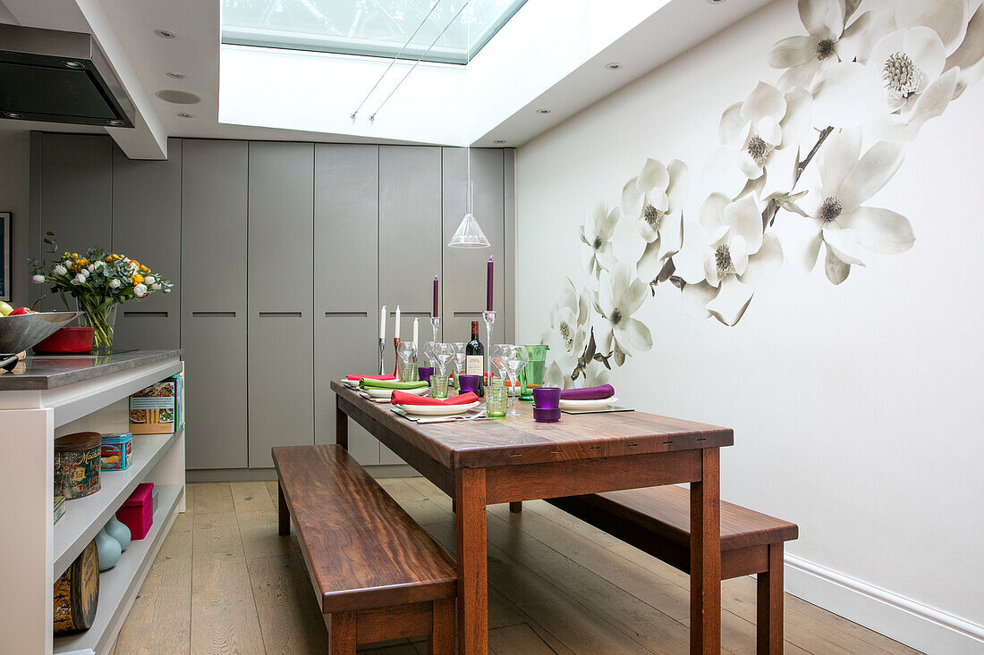 Large floral wall deco with wooden table and benches below skylight in North London kitchen UK