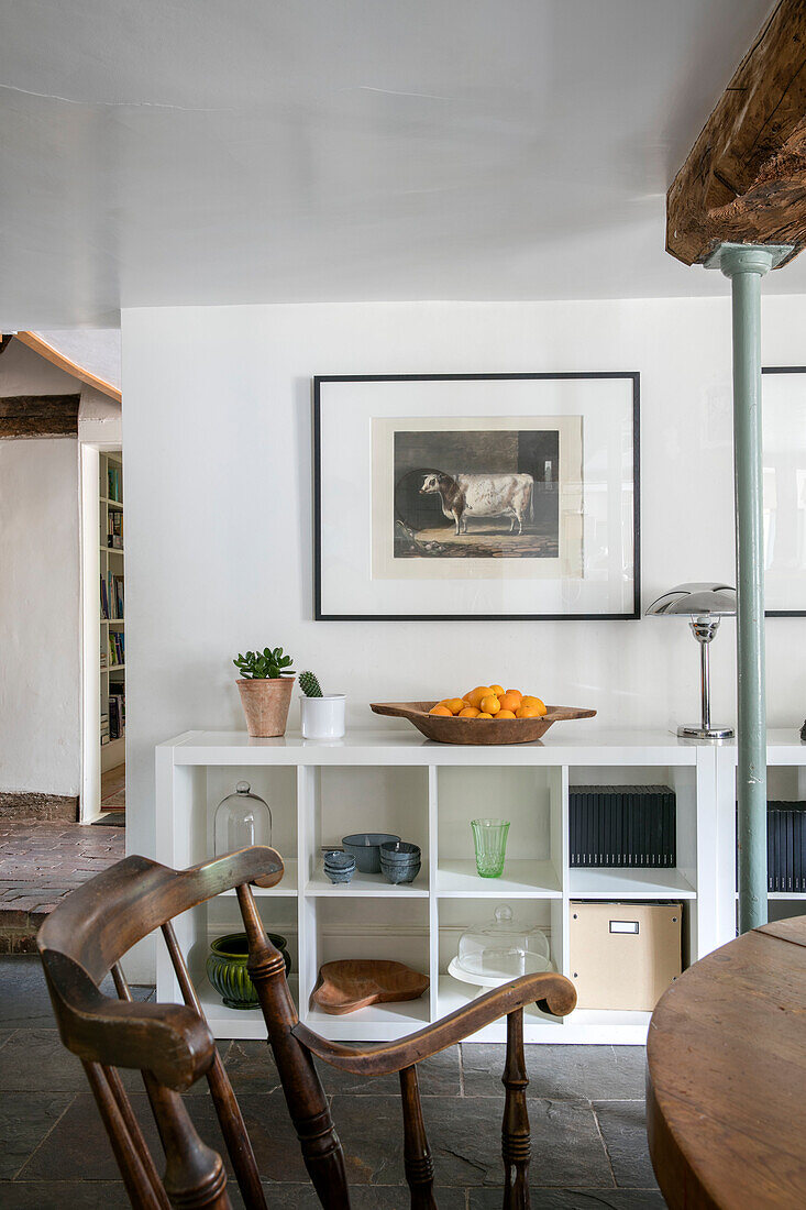 Framed print above storage shelving with old wooden chair in Kent cottage UK