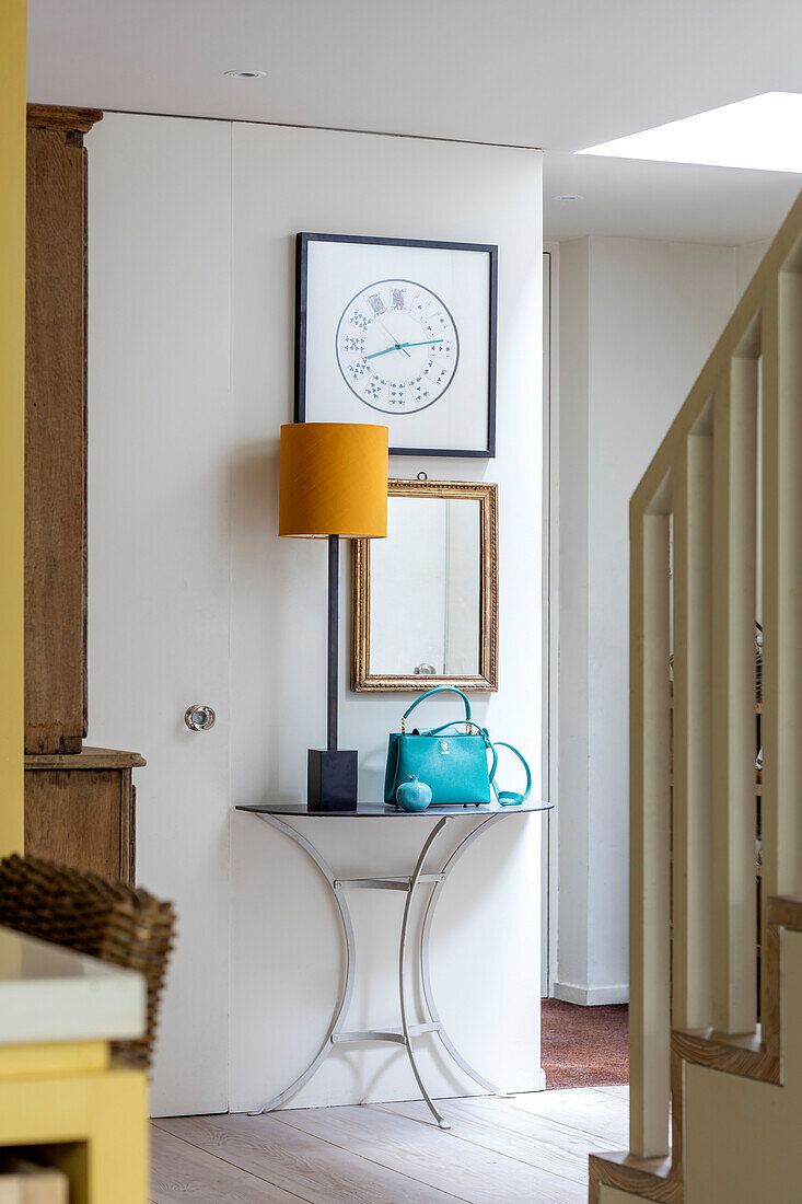 Yellow lamp and turquoise handbag on demi-lune hall table in London home UK