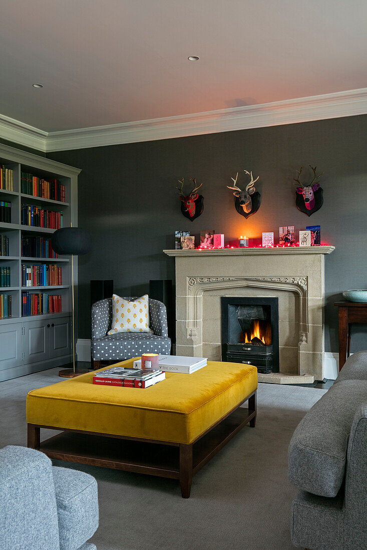 Gelber Samt-Ottoman am Kamin mit Bücherregal in einem Haus in Hampshire UK