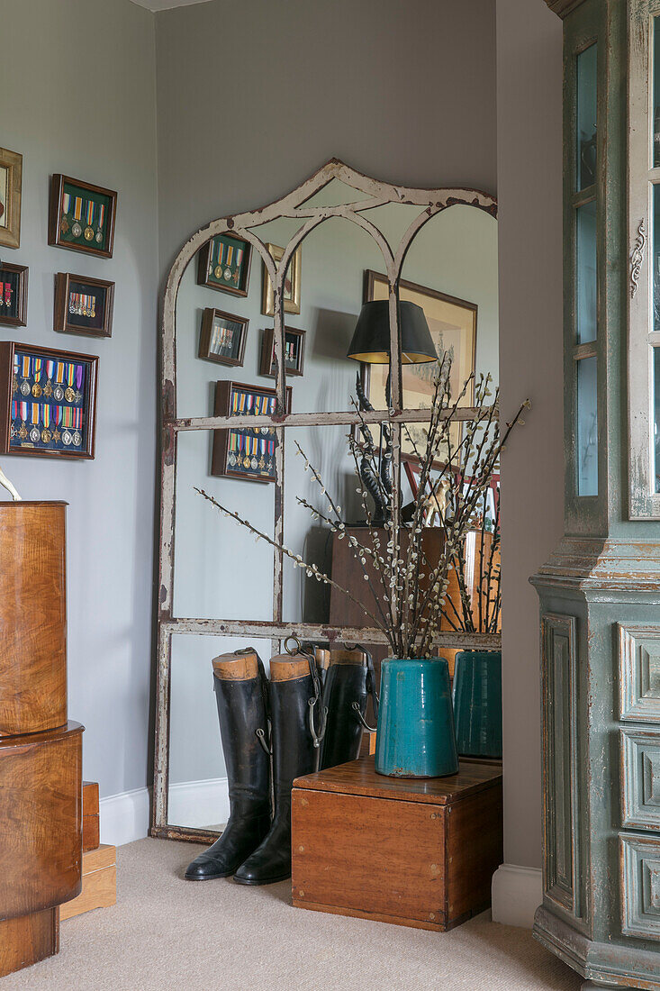 Vintage mirror and riding boots with catkins in vase on wooden box in Hampshire home England UK