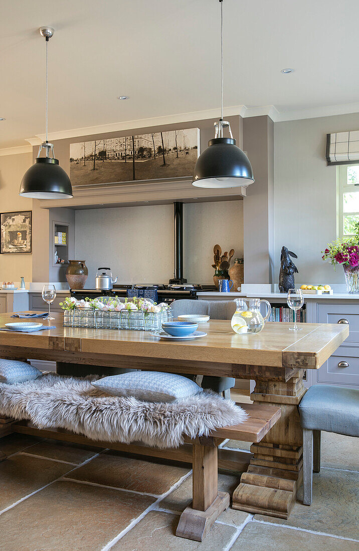 Sheepskin rug on wooden bench seat at table with black pendant shades in former Victorian coach house West Sussex UK