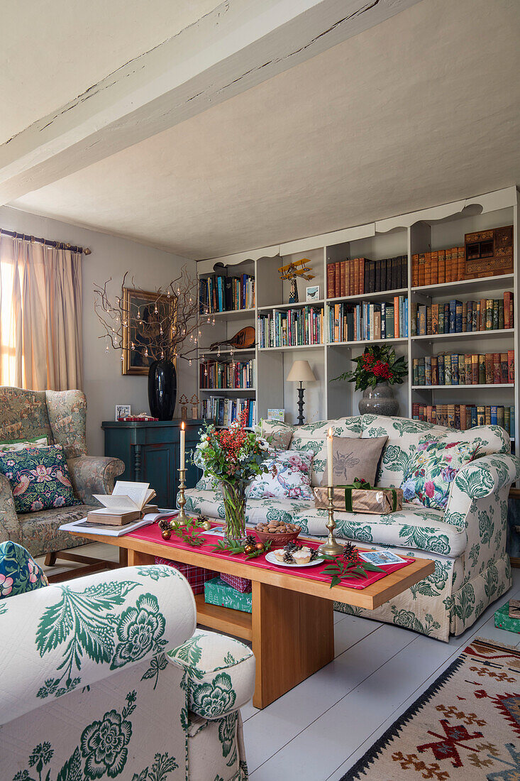 Geblümte Sofas und hölzerner Couchtisch mit Bücherregalen in einem Bauernhaus in Norfolk UK