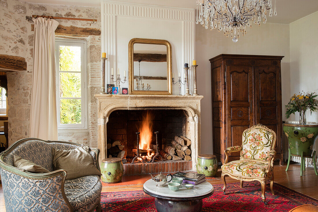 Gilt mirror above open fire with Louis XV chairs and Chinese drums in French chateau Lot et Garonne