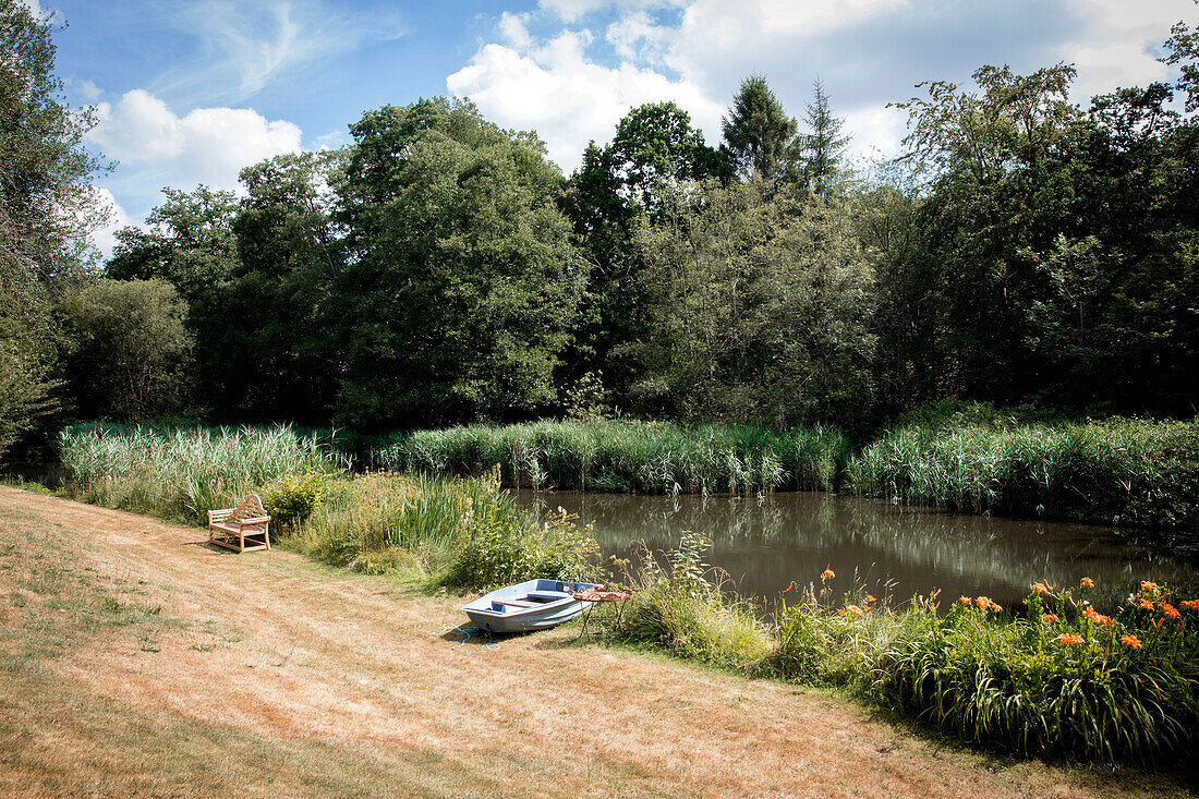 Rowing boat and bench in riverside garden of Surrey home UK
