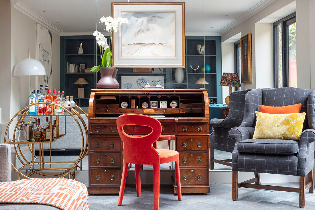 Bright red chair at 1930s rolltop desk with mirrored wall in Victorian cottage London UK