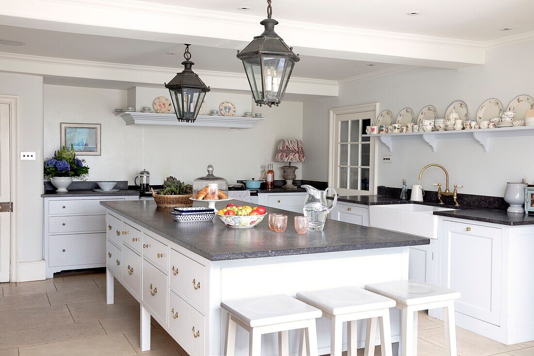 White and pale blue kitchen with dark grey worktop and open shelves filled with vintage china in elegant Hampshire home UK