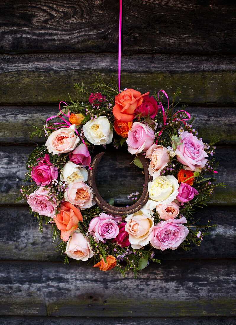 Wreath of cut roses with horse shoe hang on exterior of wood cabin in late summer