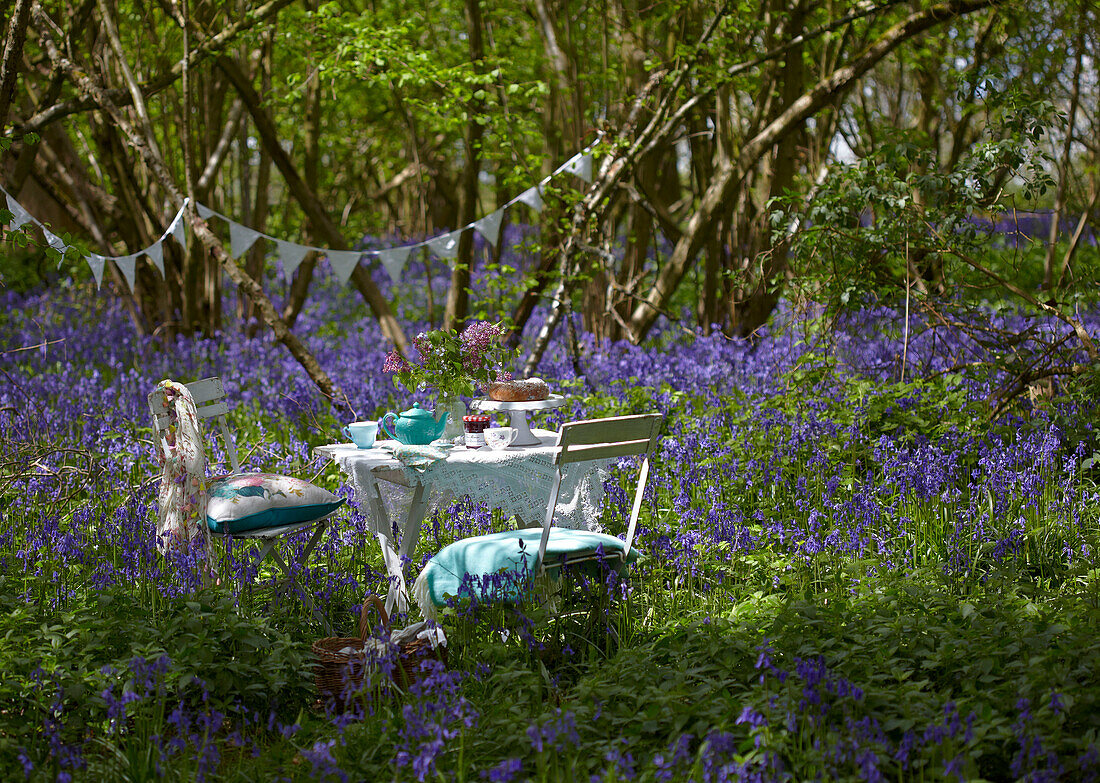 Table and chairs set for picnic with bunting in bluebell woods