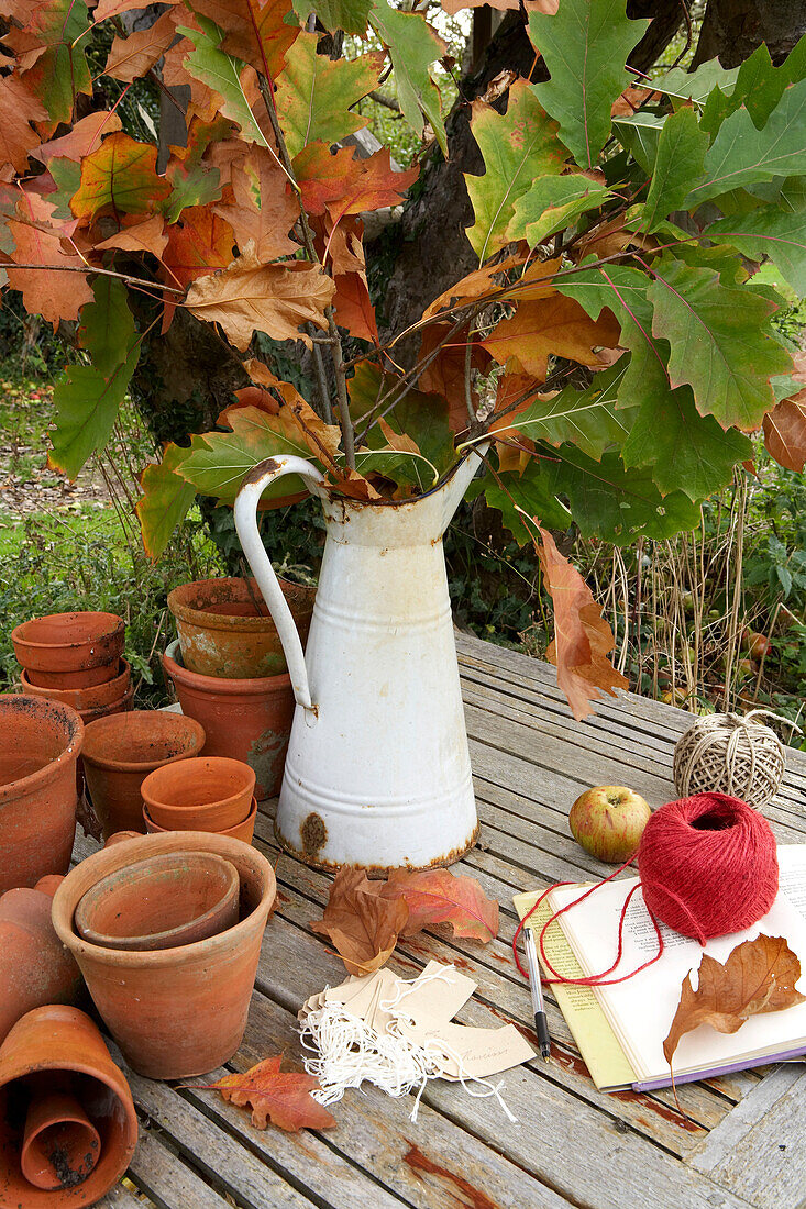 Herbstblätter in einem Metallkrug mit Terrakotta-Blumentöpfen und Schnur im Garten auf der Isle of Wight, UK