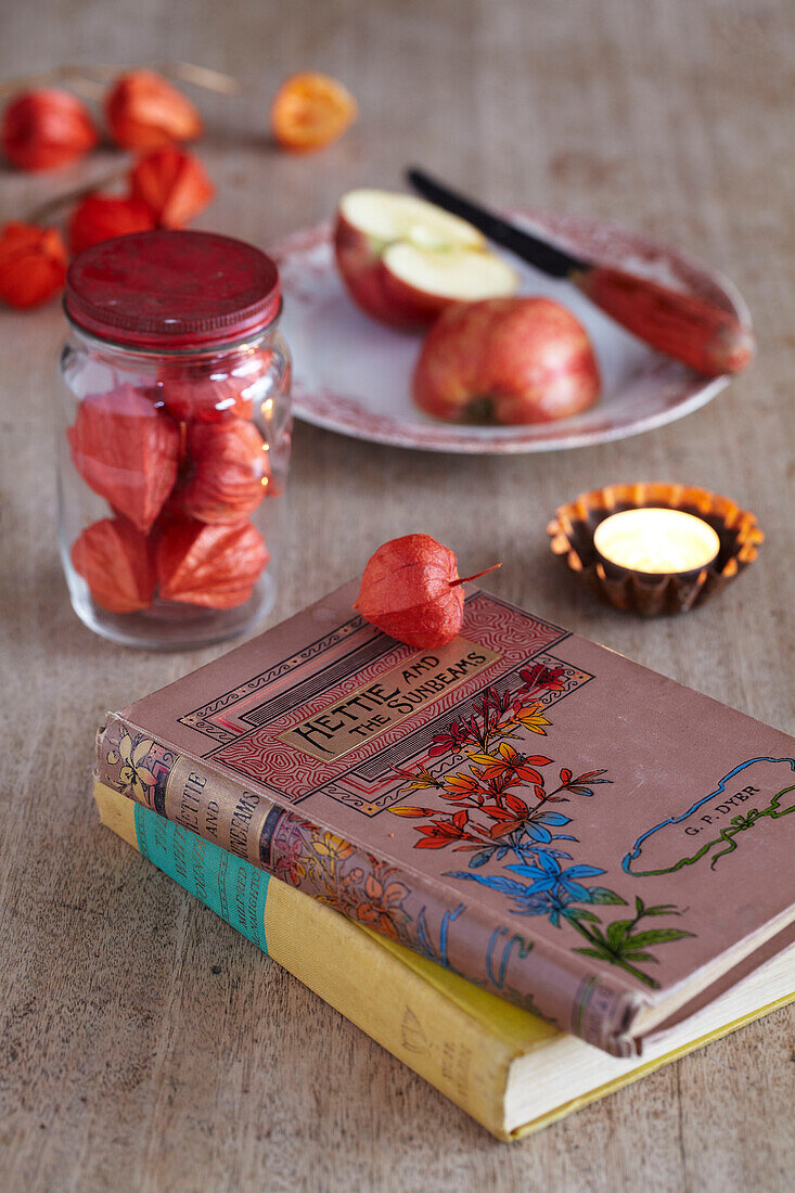 Blumenbücher im Vintage-Stil mit Teelichtern, geschnittenem Apfel auf einem Teller und einem Glas mit chinesischen Lampionblumen