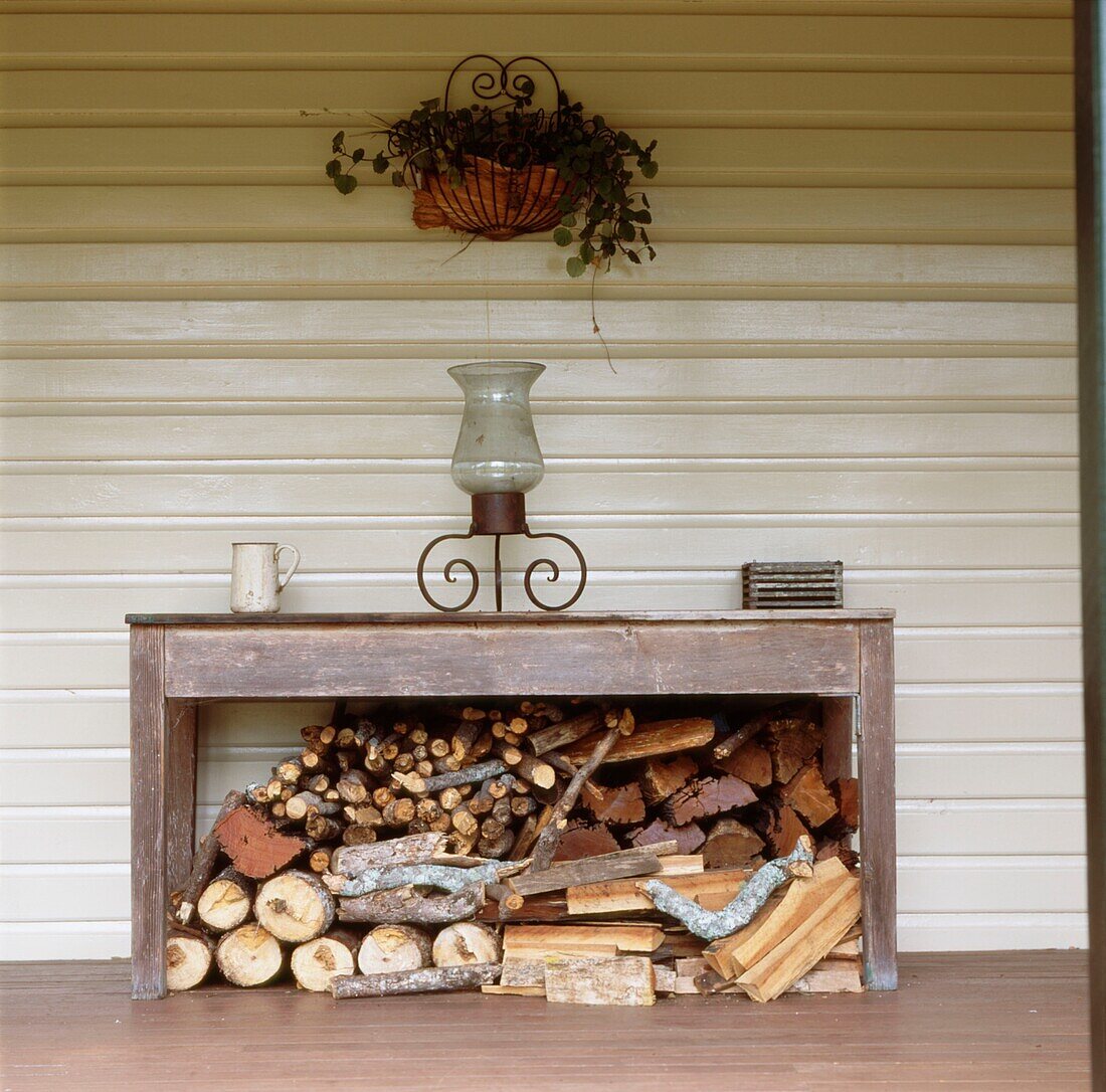 Wood panelled colonial country style house with veranda and a log pile under a table