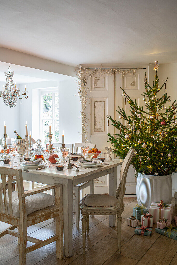 Festive table setting in dining room with decorated Christmas tree and lit candles