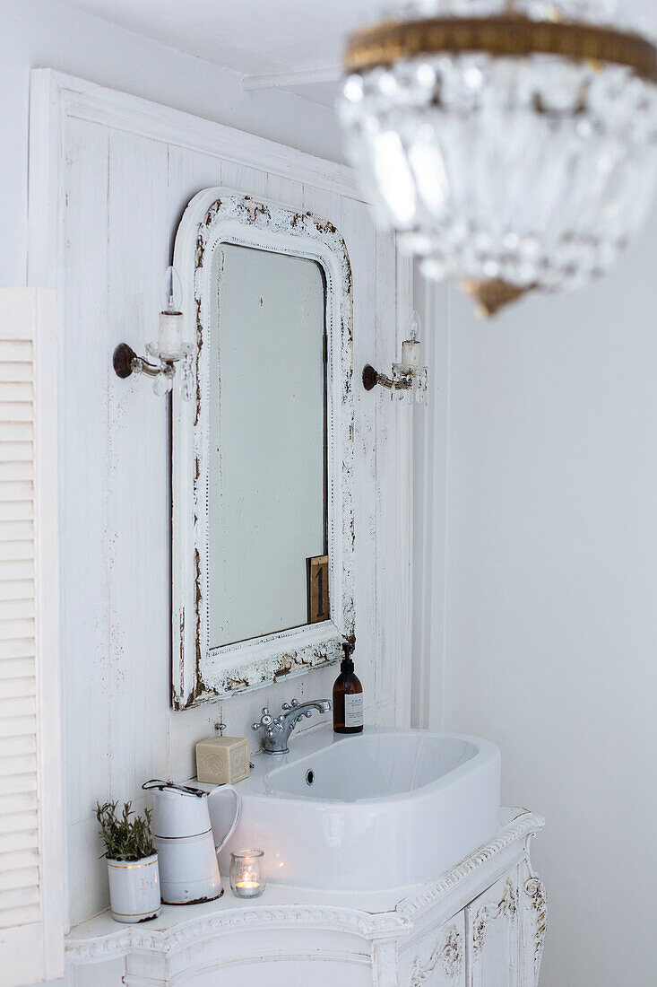 White Scandinavian style bathroom close up with ornate carved vanity unit white enamelware and pretty crystal wall lights and chandelier