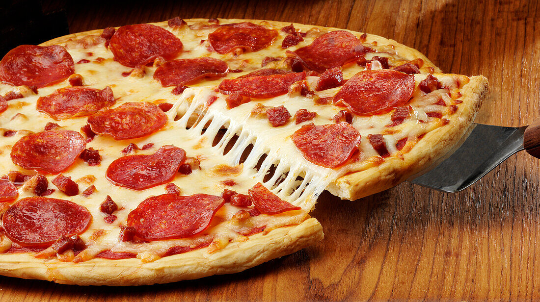 A thin crust pepperoni pizza with a slice lifted and cheese stretching