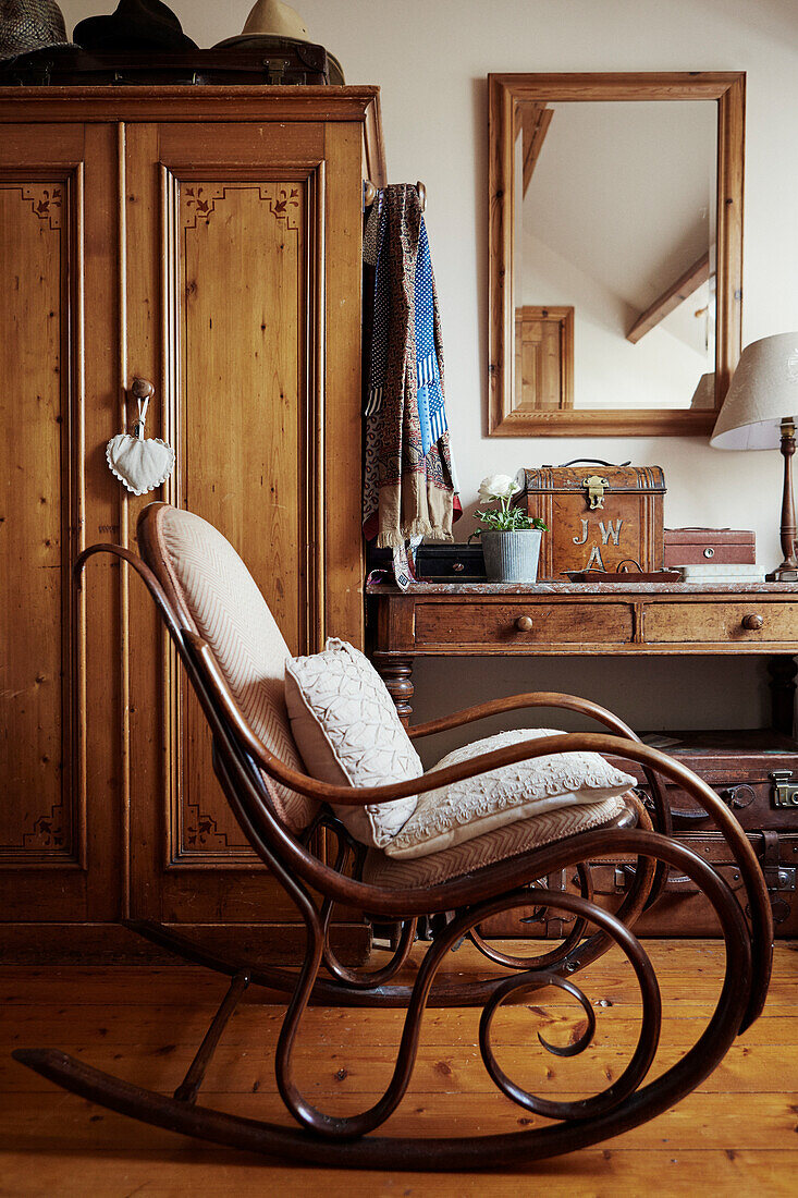 Old rocking chair in front of wardrobe and table with drawers