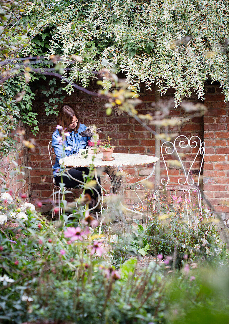 Woman with dog sitting on chair in flowering garden