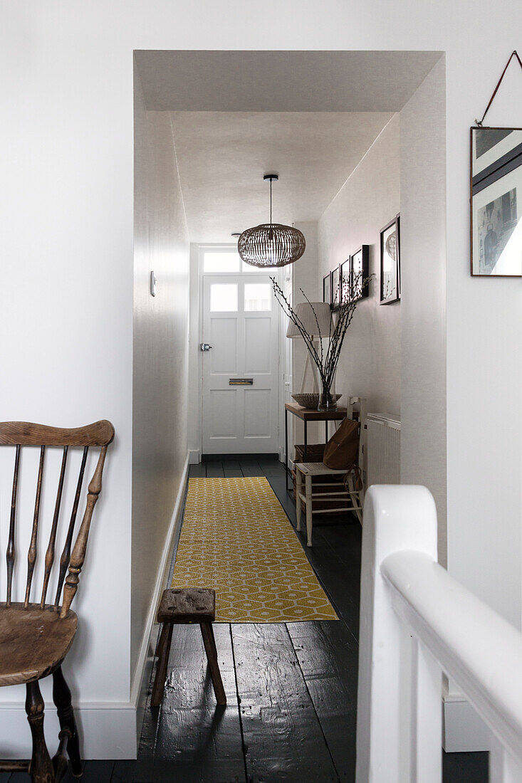 Hallway in white with black floor and yellow runner, pictures and rustic chair