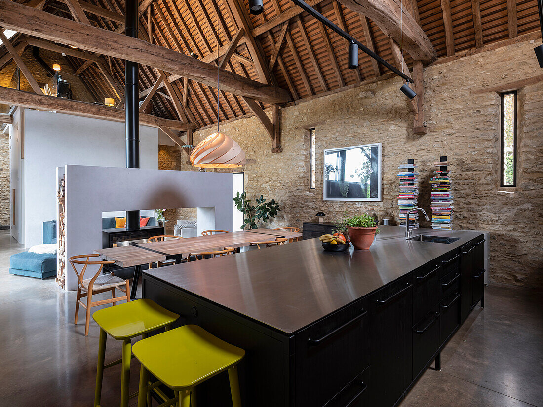 View of open plan kitchen area with large dining table and view through to double sided fire place in a former barn