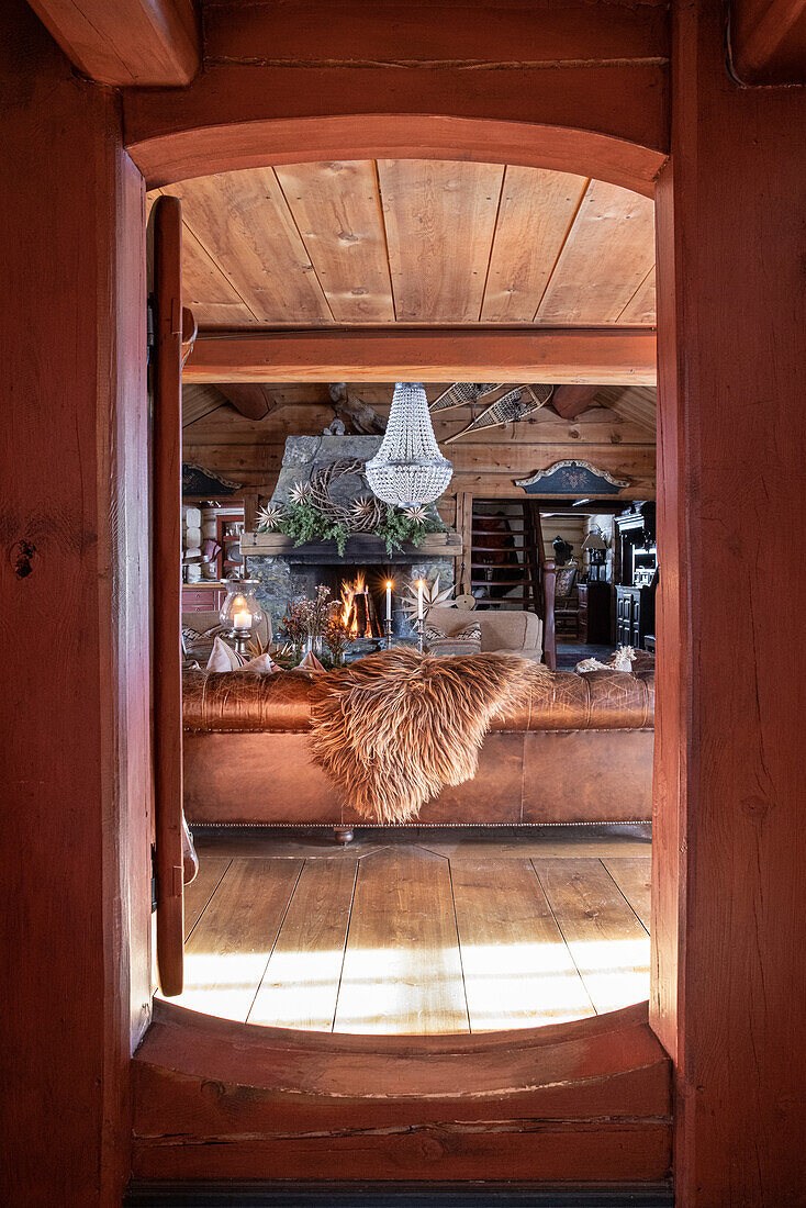 View through rustic wooden door to cosy living room with fireplace and fur decoration