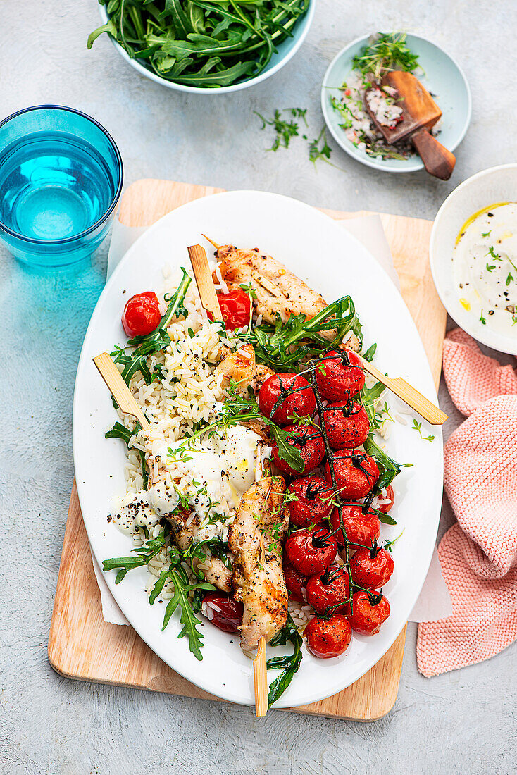 Chicken skewers on rice with baked tomatoes and rocket salad