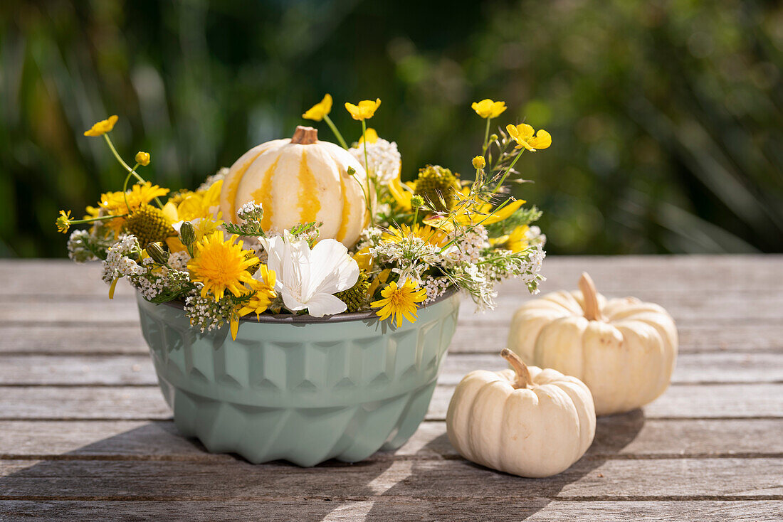 Herbstliches Arrangement aus gelben Blumen und Zierkürbissen in Kuchenform