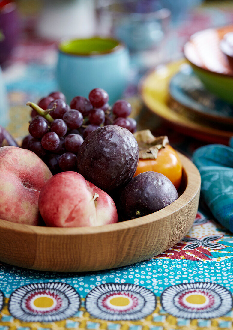 Obstschale mit Trauben und Pfirsichen auf bunt gemusterter Tischdecke