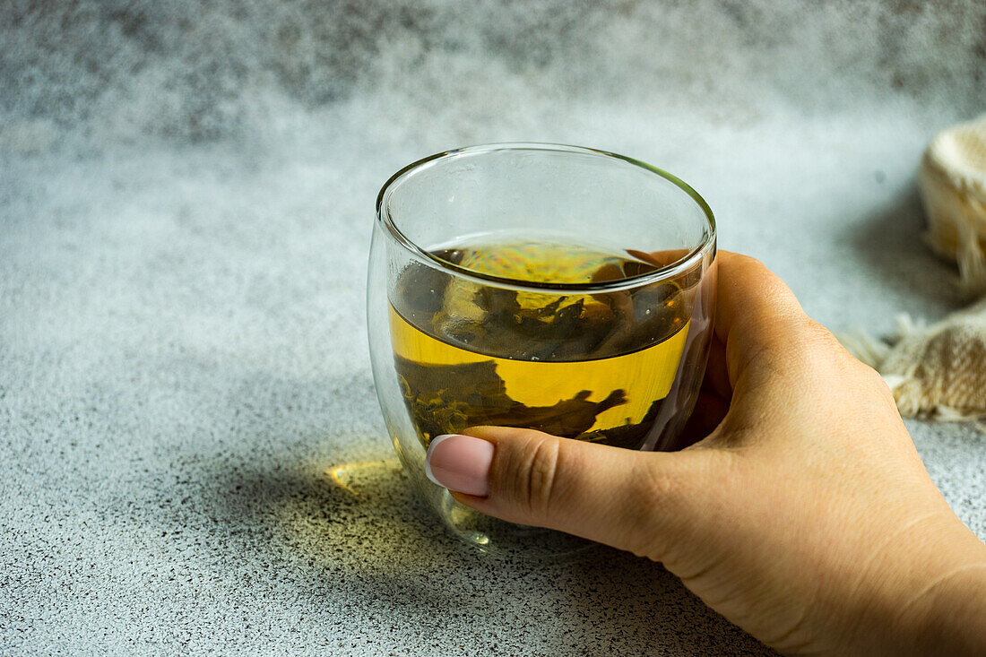 Hand hält Glas mit grünem Sencha-Tee